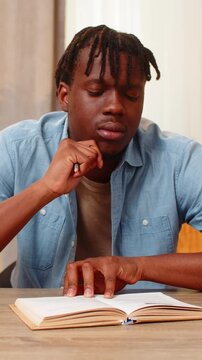 African American young man on home table studies book text marks key line and writes notes for learning and exam prep. Black boy on home table reviews lesson with focus and builds knowledge at home.