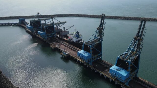 Aerial view of large industrial port with cargo cranes and a ship docked at the pier in Cilacap, Central Java, Indonesia.