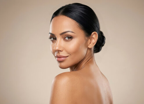 Beautiful young woman with glowing skin looking over shoulder against beige background.