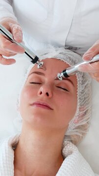 Middle-aged adult woman girl relaxes while receiving forehead-focused microcurrent therapy in modern cosmetology clinic. Procedure improves skin tone, elasticity, stimulates facial muscle activity