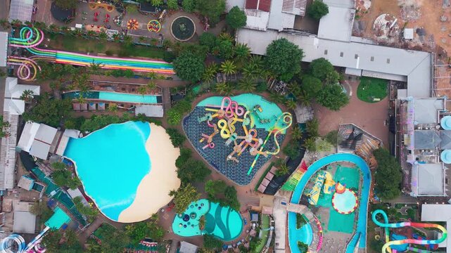 Aerial view of a colorful waterpark with multiple swimming pools, winding water slides, and lush tropical trees in Malang, East Java, Indonesia.