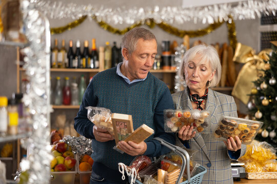 Happy elderly couple choosing products for Christmas table in supermarket - nougat, marzipan, panellets and other sweets