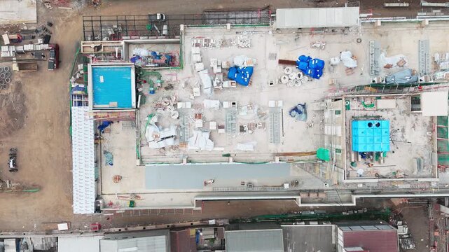 Aerial view of a construction site featuring building materials, scaffolding, and a blue tarp-covered structure in the urban area of Malang, East Java, Indonesia.