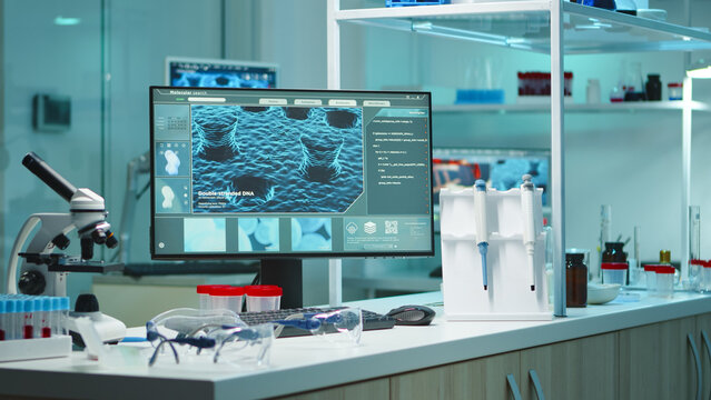 Modern molecular biology workstation with microscope, sample tubes, pipettes and a large DNA analysis display arranged for laboratory research.