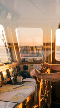 Maritime captain steering ship's wheel in control room with navigation charts and instruments visible