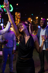 Fototapeta premium Smiling woman dances ecstatically at a New Year's Eve party, feeling emotional as she listens to music and celebrates midnight at the festive rooftop event.