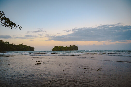 View of the coastline with a small island in the distance under a soft twilight sky, featuring calm ocean waters and a rocky shoreline in Puerto Viejo de Talamanca, Limon Province, Costa Rica.