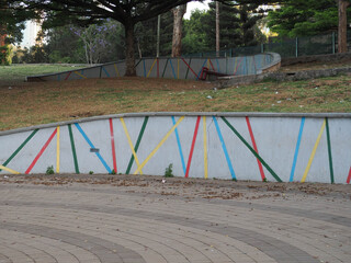 Empty Public Park with Concrete Retaining Walls Painted with Colorful Geometric Lines and Stripes, Outdoor Green Space and Paved Pathway  © Griffin9678