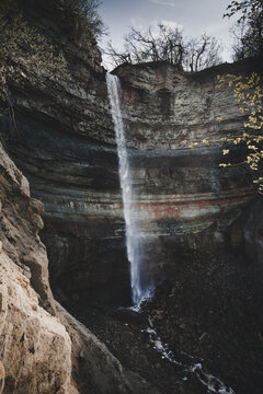 Valaste, Ida-Viru County, Estonia - 20 May 2020: View of Valaste Waterfall cascading down a dramatic limestone cliff face with layered rock strata and sparse vegetation.