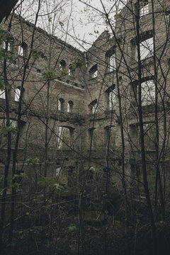 Kunda, Laane-Viru County, Estonia - 20 May 2020: View of the historic ruins of the Kunda cement factory with weathered brick walls, empty window arches, and overgrown trees.