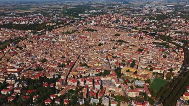 Aerial drone view of Parma, Italy, showcasing the historic city center, terracotta rooftops, churches, green spaces, urban architecture, and the Emilia-Romagna cityscape.