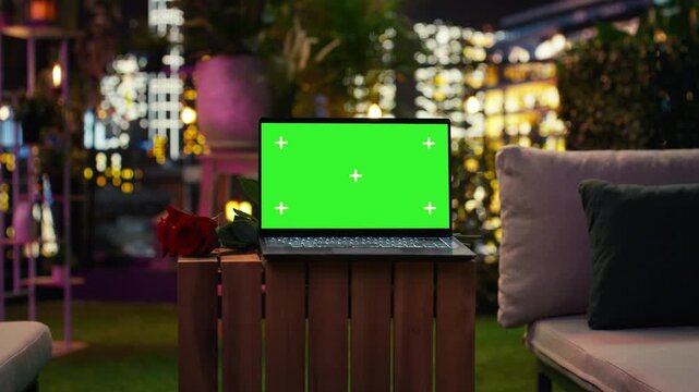 Laptop mockup sits near red roses during romantic rooftop date setup at night; A chroma key notebook sits beside red flowers beneath colorful terrace lights.