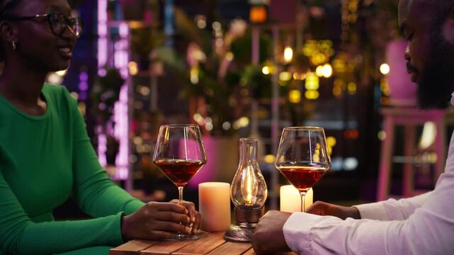 Happy couple toasts during an anniversary event at a rooftop restaurant while jolly romantic partners clink red wine glasses on the terrace with city lights behind them in close-up.