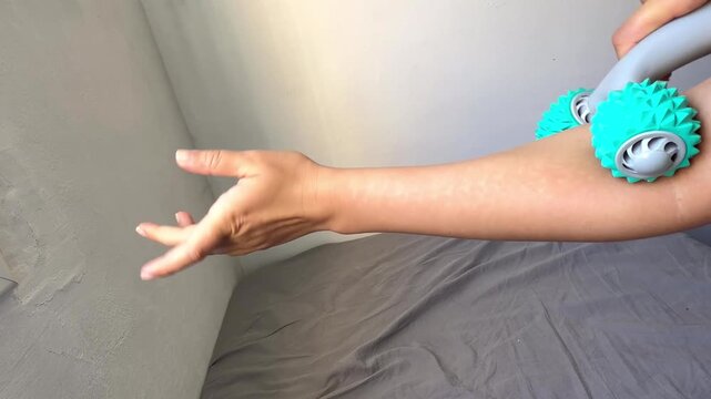 Close-up: a person massaging their forearm and hands with a handheld spiky roller massager at home to relax the muscles.