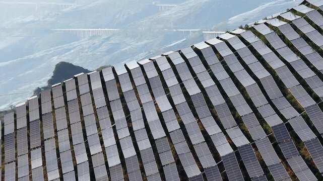 Aerial view of rows of solar panels installed on a hillside with a bridge in the background in Anshun, Guizhou, China.