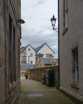 Person in a yellow coat walking down a narrow stone lane in the town of Nairn within the Highlands region of Scotland on an overcast day