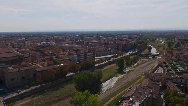 Aerial drone view of Parma, Italy, showcasing the historic city center, terracotta rooftops, churches, green spaces, urban architecture, and the Emilia-Romagna cityscape.