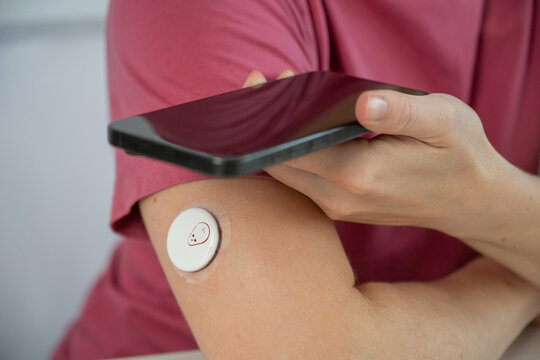 A faceless woman with a continuous glucose monitor holds a smartphone.