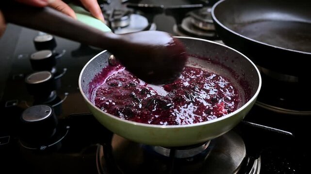 Chef stirring delicious homemade blueberry jam in pan