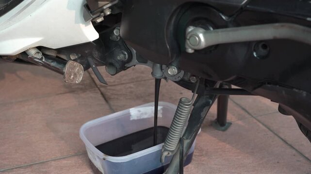Changing used engine oil on an automatic scooter at home garage.