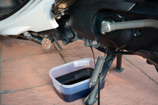 Changing used engine oil on an automatic scooter at home garage.