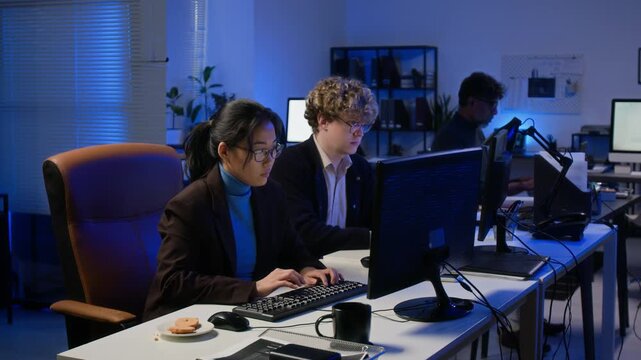 Young adult Asian woman typing on computer keyboard near Caucasian colleague in tech office. Clip suited for cybersecurity advertising, software engineering, IT commercials
