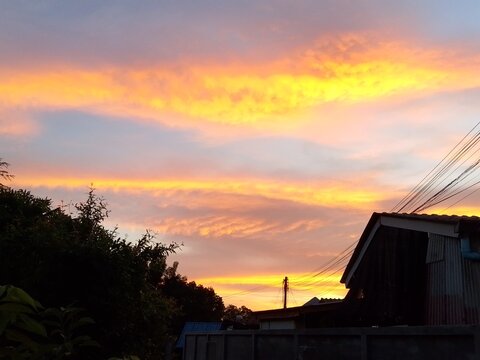 Vibrant golden hour sunset sky with glowing orange and yellow clouds over village rooftops