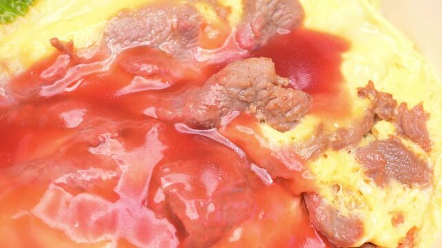 Tomato beef omelette rice with glossy red tomato sauce and tender beef slices wrapped in soft creamy omelette