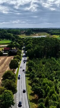 Aerial view of a road with cars passing through lush greenery and fields near the ZE PAK SA Elektrownia Patnow in Konin, Poland.