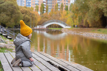 Cute toddler boy 1.5 years old sitting on wooden pier in autumn park side view © Ruslan Russland