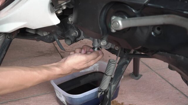 A mechanic's hand tightens the oil drain bolt during a motorcycle engine oil change in a home garage.
