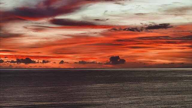 View of sunset over the ocean at Sunset Beach Tanah Lot with vibrant orange and red clouds in Kecamatan Kediri, Bali, Indonesia.