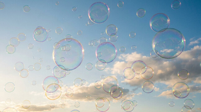 青空に舞い上がる大小のシャボン玉　雲を背景に虹色に輝く透明な泡