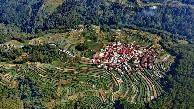 Aerial view of Pagergunung village surrounded by lush green terraced rice fields and agricultural land in Ngablak, Central Java, Indonesia.