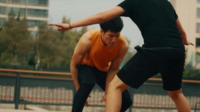 Two men play intense basketball on an outdoor court with one dribbling