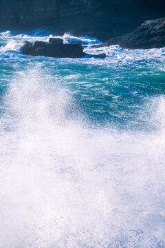View of powerful ocean waves crashing against dark coastal rocks with sea spray and turquoise water, United Kingdom.