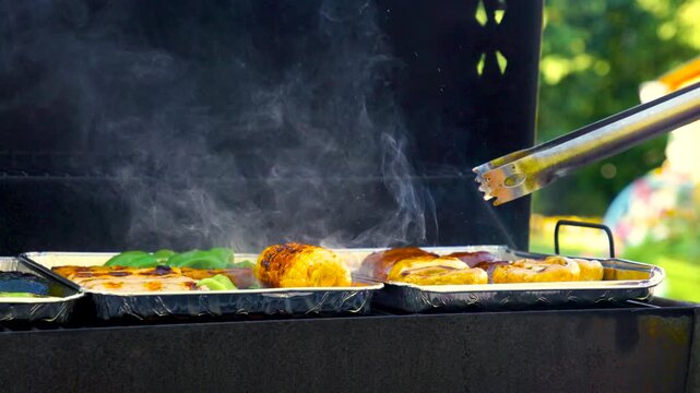 Various grilled vegetables are turned on the grill with grill tongs