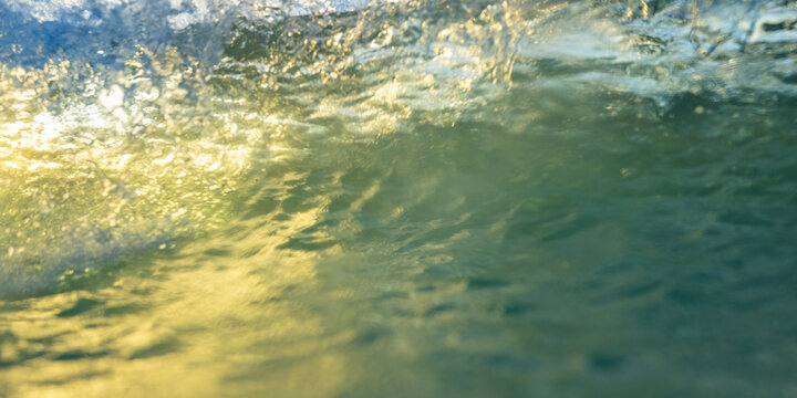 Golden sunset light filtering through an abstract ocean wave in motion
