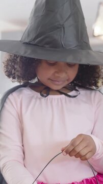 Vertical video: Hearing call, girl in witch hat checking bucket for candy at home with blue lolly