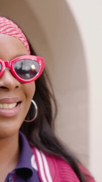 Vertical video: Smiling woman adjusting cat shades, peeking in jacket at arch as camera pulls back
