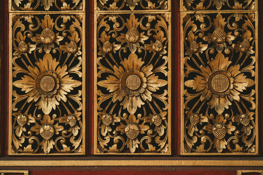 View of intricate traditional Balinese wood carvings with floral motifs and gold leaf detailing on a dark wooden panel in Ubud, Bali, Indonesia.