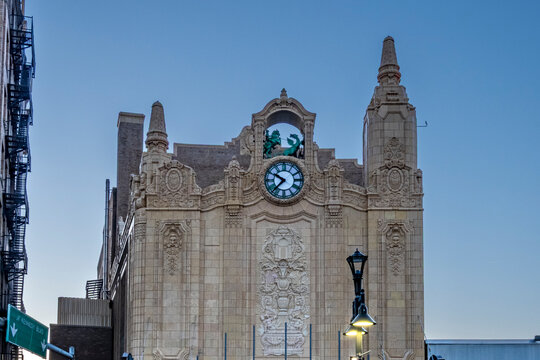 Jersey City, NJ - US - Oct 7, 2026 : An ornate clock and sculpted figures crown the Loew's Jersey Theatre in Journal Square, with ornate carved stone ornament and streetlights beneath the evening sky.