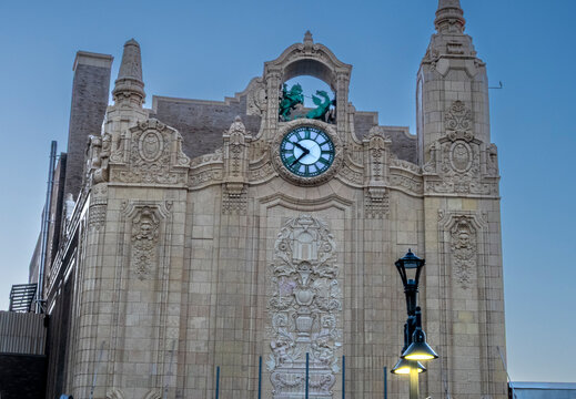 Jersey City, NJ - US - Oct 7, 2026 : The ornate facade of Loew's Jersey Theatre features a Roman numeral clock, sculpted figures, stone carvings and decorative high towers beneath a clear evening sky.