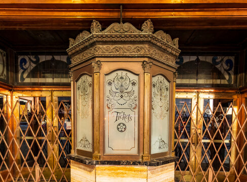 Jersey City, NJ - US - Oct 7, 2026 : An ornate ticket booth at the historic Stanley Theater features etched glass panels, gilded trim and marble beneath a warmly lit entrance with metal security gate.