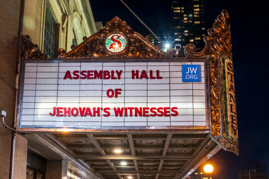 Jersey City, NJ - US - Oct 7, 2026 : An illuminated marquee at the Stanley Theater displays Assembly Hall of Jehovah's Witnesses signage, surrounded by decorative metal scrollwork and stained glass