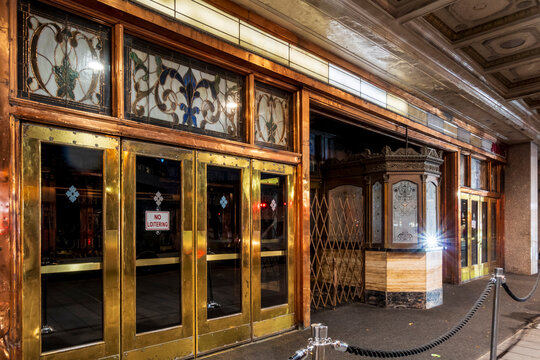 Jersey City, NJ - US - Oct 7, 2026 : The Stanley Theater entrance features brass-framed glass doors, decorative stained glass transoms, an ornate ticket booth and a patterned canopy ceiling at night..