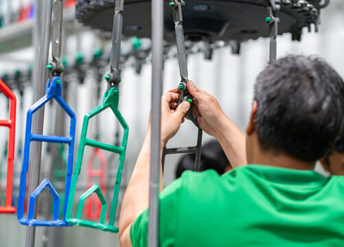 Close-up of a worker in a green shirt calibrating machinery hangers on an industrial production line.