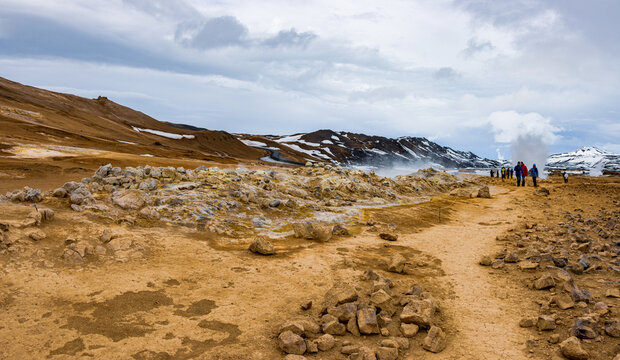 View of Hverir Sulfur Springs with steaming fumaroles, bubbling mud pools, and volcanic terrain under a cloudy sky with tourists in Reykjahlid, Thingeyjarsveit, Iceland.