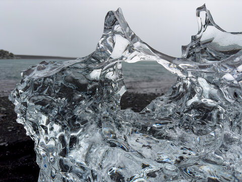 View of a clear ice formation from a melting glacier on the black sand beach at Diamond Beach, Sveitarfelagid Hornafjordur, Iceland.