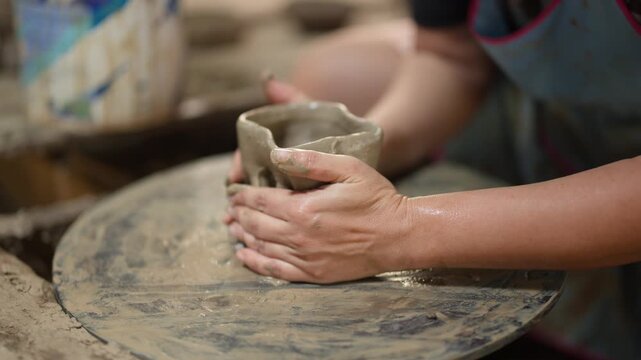Asian Artisan Shaping Clay Vessel on Pottery Wheel in Workshop